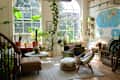 Bright living room filled with various indoor plants, a green armchair, a light brown ottoman, and a world map on the wall.