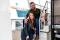 Couple sitting on a boat with a dog, surrounded by festive string lights.