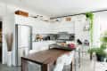 Modern kitchen with white cabinets, stainless steel fridge, wooden dining table, and plants.