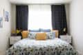 Bedroom with floral bedding, yellow and blue pillows, dark curtains, and white nightstands with decor items.