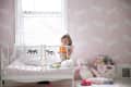Toddler in a crib with pink rabbit wallpaper, surrounded by stuffed animals and toys.