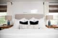 Bedroom with a beige headboard, white and black pillows, wooden side tables, and blue lamps.