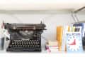 Vintage Underwood typewriter on a shelf beside stacked books and a "Will Return" clock sign.
