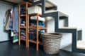 Under-stair storage with wooden shelves, folded clothes, hanging garments, and a woven basket on a tiled floor.