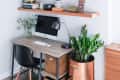 Home office with wooden desk, black chair, computer, and shelves displaying books, plants, and decorative items.