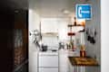 Small kitchen with white cabinets, brick wall, hanging utensils, knife rack, and a blue phone sign.