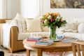 Cozy living room with a beige sofa, patterned pillows, a wooden coffee table, and a vase of colorful flowers.