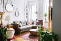 Cozy living room with gray sofa, colorful pillows, round wooden table, plants, and decorative mirrors on white brick wall.