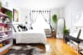 Bright bedroom with white bedding, black and white curtains, a full-length mirror, plants, and a bookshelf with decor.