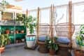 Rattan chairs with blue cushions on a balcony, surrounded by potted plants and bamboo fencing.