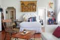 Cozy bedroom with a tufted headboard, colorful pillows, wooden chair, and a tapestry above the bed.