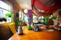 Eclectic room with hanging plants, yellow chair, wooden table, kettle, and colorful decor under draped fabric ceiling.