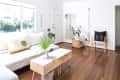 Bright living room with white sofa, wooden floor, potted plants, and a modern chair with a black cushion.