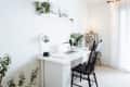 Home office with a white desk, laptop, black chair, plants, and decorative shelf in a bright room.