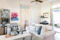 Living room with white sofa, patterned cushions, floral artwork, blue vases, and a ceiling fan.