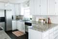 Modern kitchen with white cabinets, granite countertops, stainless steel fridge, and black tile floor.