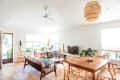 Bright living room with wooden furniture, a TV, large windows, and a woven pendant light.