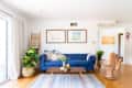 Blue tufted sofa with patterned pillows, wooden coffee table, hand-shaped chair, and potted plants in a bright living room.