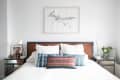 Bedroom with wooden headboard, white bedding, blue and red accent pillows, mirrored nightstands, and framed artwork above.