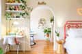Bedroom with red bed frame, white desk, plants, and archway leading to a room with a blue chair and wall decor.