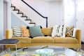 Beige sofa with geometric patterned cushions in a living room, near a staircase with black railing.