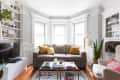 Living room with a gray sofa, yellow pillows, coffee table, TV, shelves, and large windows.