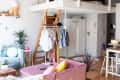 Loft apartment with a wooden ladder, clothing rack, pink sofa, and plants, featuring a cozy and eclectic decor style.