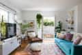 Bright living room with blue sofa, colorful rug, plants, and open doors to patio.