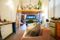 Loft apartment with a vintage van under a wooden mezzanine, pink sofa, and plants.