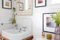 Bathroom with vintage sink, distressed mirror, framed art, green vase, and candles on a white shiplap wall.