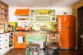 Retro kitchen with orange appliances, green accents, wooden island, and eclectic decor.