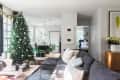 Living room with a decorated Christmas tree, gray sectional sofa, and dining area with green chairs in the background.