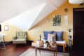 Attic living room with floral armchair, blue cushions, potted plants, and wall art on a slanted ceiling.