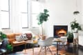 Cozy living room with a leather sofa, white chairs, plants, and a lit fireplace.