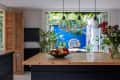 Kitchen island with fruit bowl, flowers, and pendant lights, overlooking a patio with plants and a wicker chair against a blue wall.