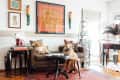 Living room with a brown sofa, dog, colorful artwork, and eclectic decor on a red patterned rug.