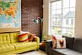 Living room with a yellow sofa, colorful pillows, world map, and a gray couch by a large window.