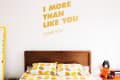 Bedroom with wooden headboard, polka dot bedding, wall quote "I more than like you. I love you," and orange side table.