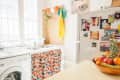 Colorful kitchen with a patterned curtain under the sink, fruit bowl on the counter, and photos on the fridge.