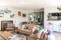 Mid-century modern living room with beige sofa, armchairs, fireplace, and birch tree wallpaper, featuring plants and decor.