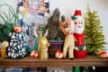 Festive shelf with Santa, reindeer, angel figurines, colorful ornaments, and small Christmas trees.
