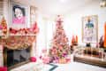 Festive living room with a decorated Christmas tree, colorful garlands on the fireplace, and wrapped gifts.