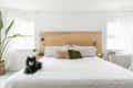 Bedroom with a wooden headboard, white bedding, green and pink pillows, and a small black dog on the bed.