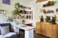 Home office with wooden desk, bookshelves, potted plants, and a gray sofa with cushions.