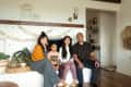 Family of four sitting on a white stone fireplace ledge, with plants and wall decor in a cozy living room.