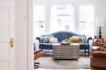 Blue velvet sofa with patterned cushions, wooden coffee table, and leather armchair in a bright living room.