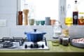 Blue Dutch oven on a gas stove, surrounded by jars, spices, and cooking oils on a kitchen counter.
