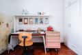 Home office with wooden chair, desk, pink tool chest, clipboards on wall, and shelf with vases and decor items.