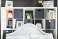 White cubby shelf with black baskets, books, a globe, salt lamp, and a plant behind a tufted headboard.