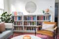 Living room with bookshelves, a round mirror, a leather chair, a plant, and a "Good Vibes Only" sign.